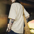 Person wearing a beige oversized t-shirt with a tattoo on their arm, holding a brown bag.